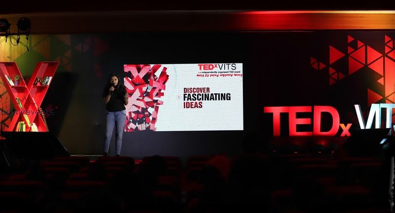 The TEDxVITS stage with a speaker under red staging and a giant X